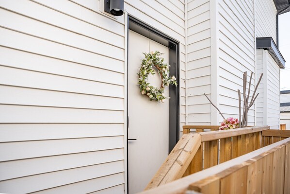 A white building with horizontal siding, a wooden deck, and a wreath on the door. - Cozy, modern suite in trendy, historic Hazeldean. Close to Whyte/UofA
(Edmonton)