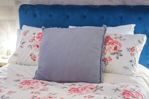 A bed with a blue upholstered headboard, floral-patterned bedding, and two pillows. - Cozy, modern suite in trendy, historic Hazeldean. Close to Whyte/UofA
(Edmonton)