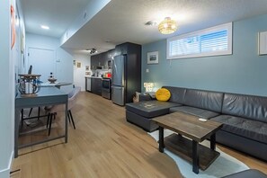 A modern kitchen with dark cabinets, a refrigerator, and a dining area with a table and chairs. - Cozy, modern suite in trendy, historic Hazeldean. Close to Whyte/UofA
(Edmonton)