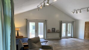 A spacious living room with a high ceiling, a leather armchair, a small table, and a billiard table. There are two sliding glass doors leading to a patio area.