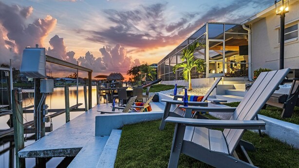 Ein Außenbereich mit Lounge-Möbeln und Tischen, mit Blick auf ein Gewässer und einen Sonnenuntergang.