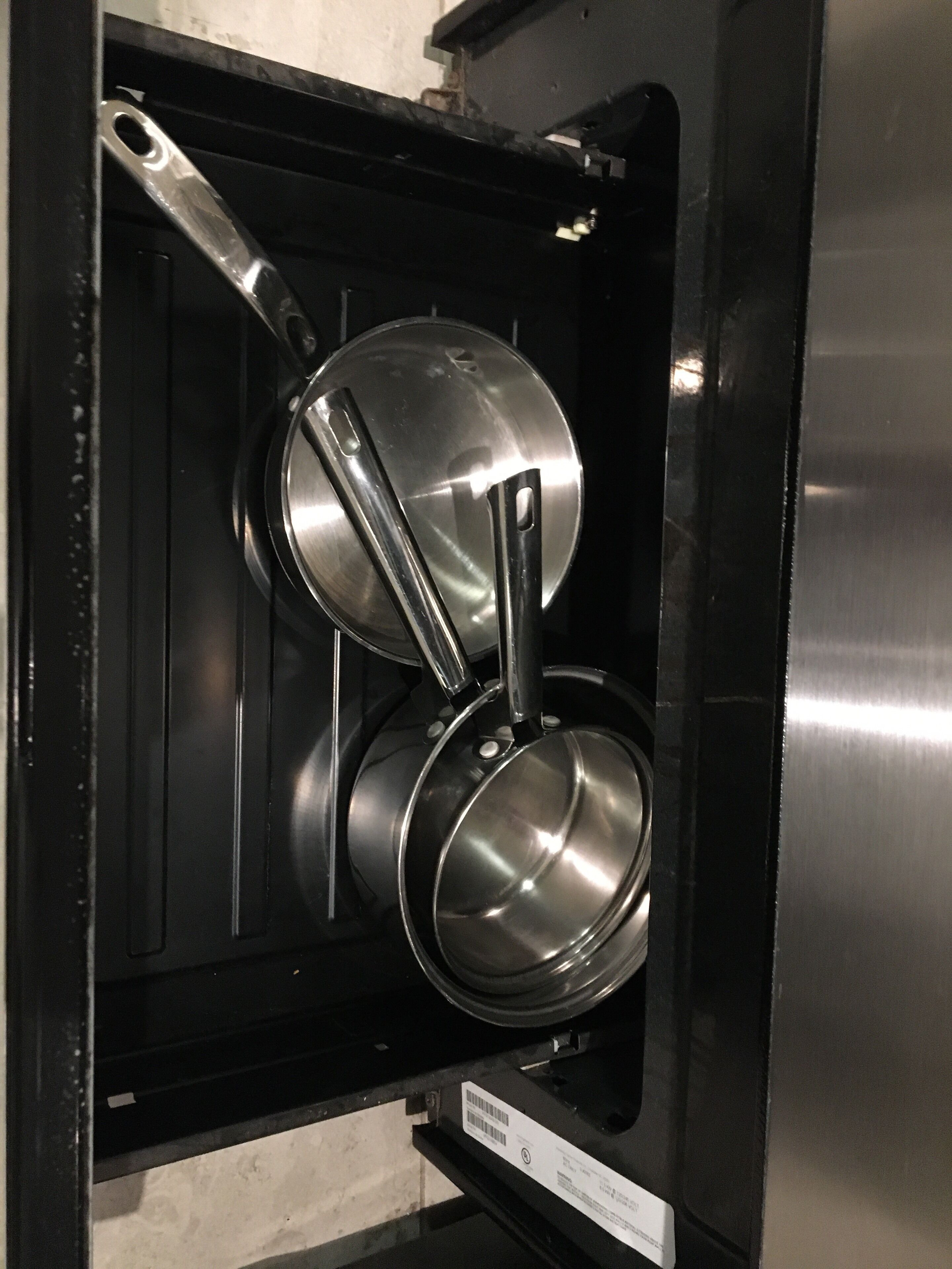A stainless steel pot and pan set inside a black cabinet.
