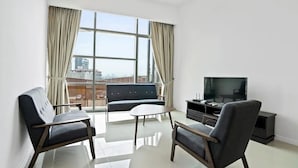 A modern living room with a sofa, two armchairs, a coffee table, and a TV. Large windows offer a city view. - Deluxe2 Paradigm Mall (Petaling Jaya)
