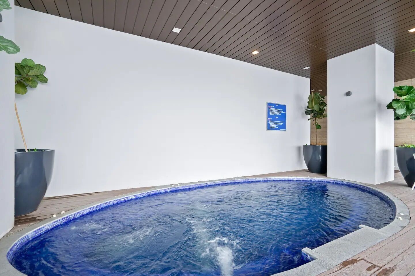 Ein moderner, überdachter Pool mit klarem, blauem Wasserspiel, umgeben von weißen Wänden und Holzböden.