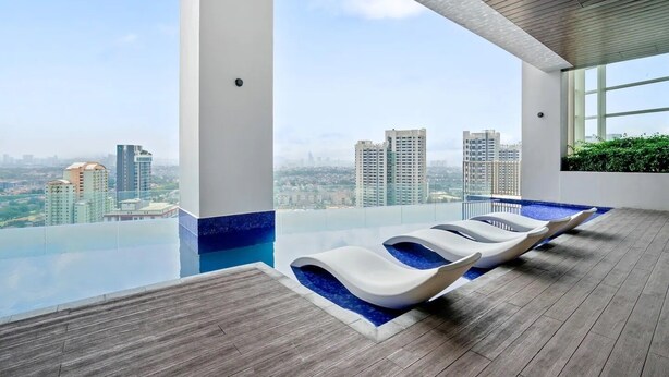 An infinity pool with lounge chairs, a wooden deck, and a city view. - Deluxe2 Paradigm Mall (Petaling Jaya)