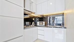 A modern kitchen with white cabinetry, a built-in microwave, and a sleek countertop. - Deluxe2 Paradigm Mall (Petaling Jaya)