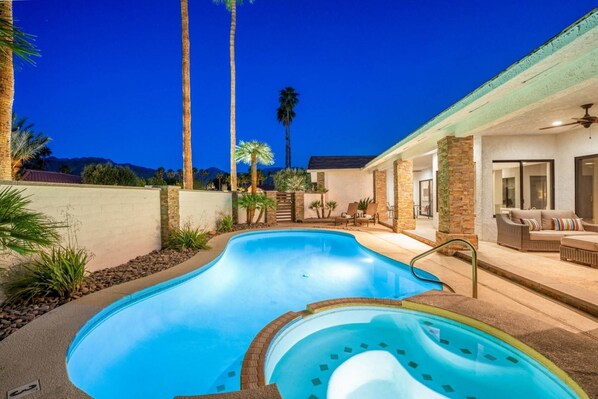 Ein Pool mit Whirlpool, umgeben von einer Terrasse mit Gartenmöbeln und Palmen.