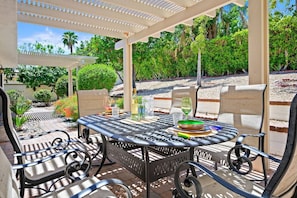 Une terrasse extérieure avec une table et des chaises rondes en métal, entourée de verdure et agrémentée d’une pergola.
