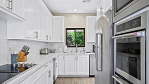 A modern kitchen with white cabinetry, stainless steel appliances, and a window with a view of greenery.