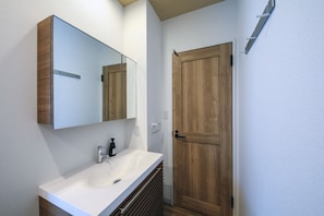 A bathroom with a white sink, a mirror, and a wooden door. - HOTEL R9 The Yard Miyakojima (Miyakojima)