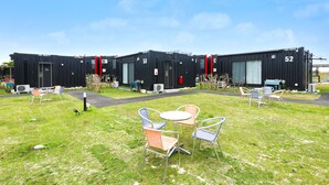 A row of black modular buildings numbered 52 and 53, each with a small patio area featuring metal chairs and a table. - HOTEL R9 The Yard Miyakojima (Miyakojima)