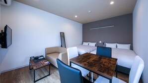 A modern hotel room with a bed, a sofa, a wooden table, and a TV on the wall. - HOTEL R9 The Yard Miyakojima (Miyakojima)