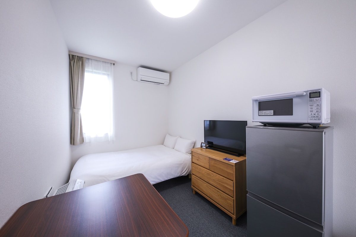 A hotel room with a bed, a wooden dresser, a microwave, and a television.