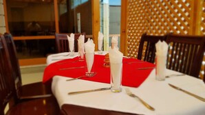 Een eettafel gedekt met witte servetten, glazen en bestek, onder een rode tafelkleed.