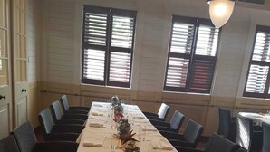 Een lange eettafel met een witte tafelkleed en een rode loper, omringd door donker beklede stoelen.
