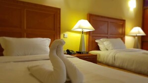 Een hotelkamer met twee bedden, elk voorzien van een houten hoofdeinde, een nachtkastje met een lamp en een handdoek in de vorm van een zwaan op het bed op de voorgrond.