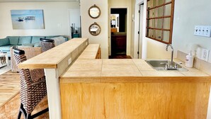 Una cocina moderna con una isla central, un área de comedor con un sofá azul y un pasillo que lleva a otras habitaciones.