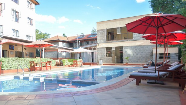 A swimming pool with sun loungers and umbrellas, surrounded by buildings with balconies and a clear sky. - Homes by Della (Nairobi)