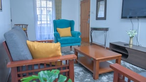 A living room with a sofa, armchair, coffee table, TV, and a door. - Homes by Della (Nairobi)