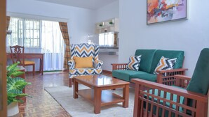 A living room with a wooden coffee table, a green sofa, and a patterned armchair. - Homes by Della (Nairobi)