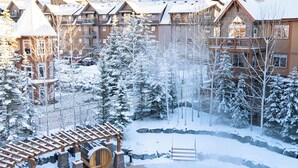A resort with a pool surrounded by snow-covered trees and mountains in the background. - Stoneridge 303 | Heated Outdoor Pool & Hot Tub (Canmore)