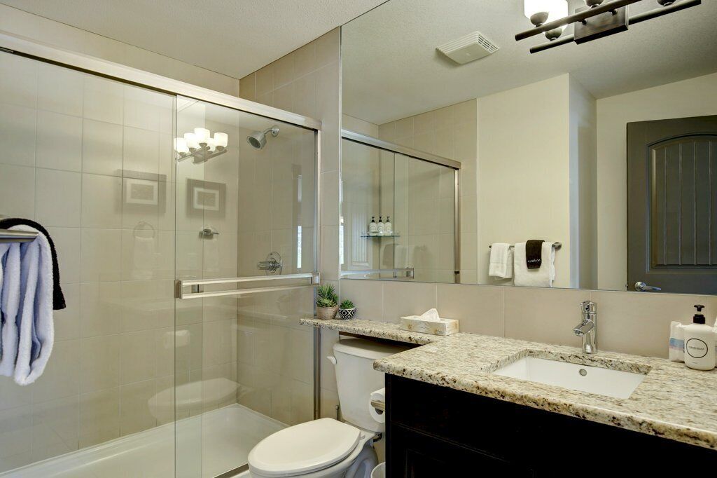 Un baño moderno con ducha envuelta en vidrio, lavamanos con encimera de granito y retrete.