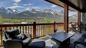 A covered outdoor seating area with wicker furniture and a view of snow-capped mountains. - Stoneridge 303 | Heated Outdoor Pool & Hot Tub (Canmore)