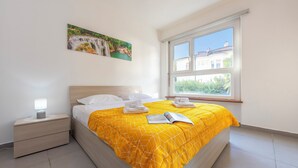 A bedroom with a bed, a nightstand, a window, and a painting on the wall. - City Apartment With Balcony and Parking (Lugano)