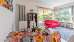 A dining area with a table set for four, a red sofa, and a view of greenery outside. - City Apartment With Balcony and Parking (Lugano)