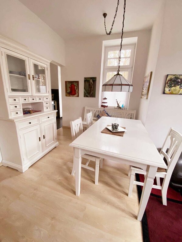 A dining area with a white table and chairs, a white cabinet with drawers, and a hanging light fixture.