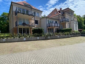 A two-story residential building with balconies, a paved driveway, and a landscaped garden area.