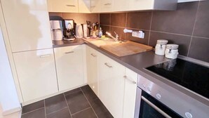 A modern kitchen with white cabinets, a black stove, and a tiled floor. - Vacation apartment Bucheneck 2 (Graal-Müritz)