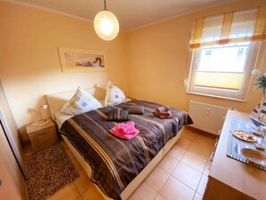 Quarto com cama, mesa de cabeceira, abajur e janela com persianas.
