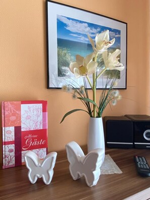 Uma mesa com um vaso de flores, um quadro emoldurado, um livro e figuras decorativas de borboletas.
