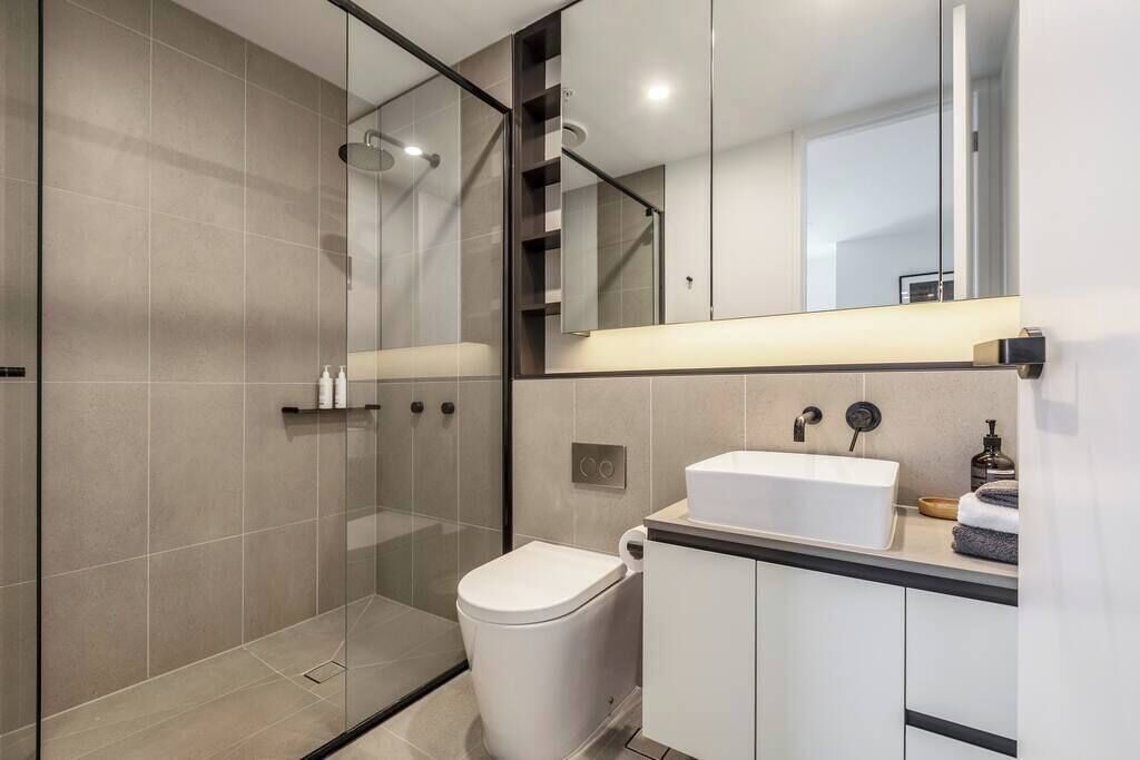 Un baño moderno con cabina de ducha de vidrio, inodoro blanco y tocador con lavamanos.