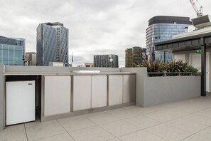 Un espace moderne sur le toit, comprenant un coin cuisine, un petit réfrigérateur et une vue sur les immeubles environnants.