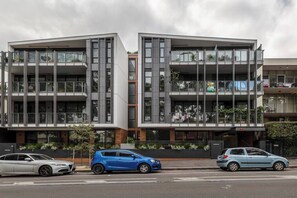 A modern building with multiple balconies, large windows, and a parking area with cars. - Modern & Eclectic 2 Bed/2 Bathroom - No Carpark (North Melbourne)