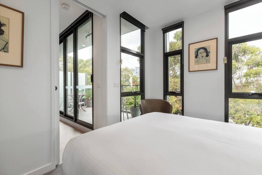 A bedroom with a large bed, a chair, and multiple windows offering views of the outdoors.