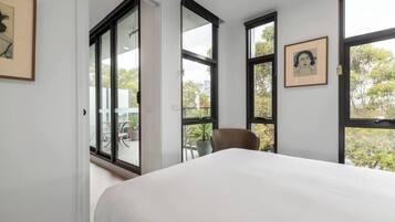 A bedroom with a large bed, a chair, and multiple windows offering views of the outdoors.