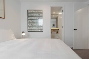 A bedroom with a large bed, a bedside lamp, a framed picture on the wall, and a door leading to a bathroom.