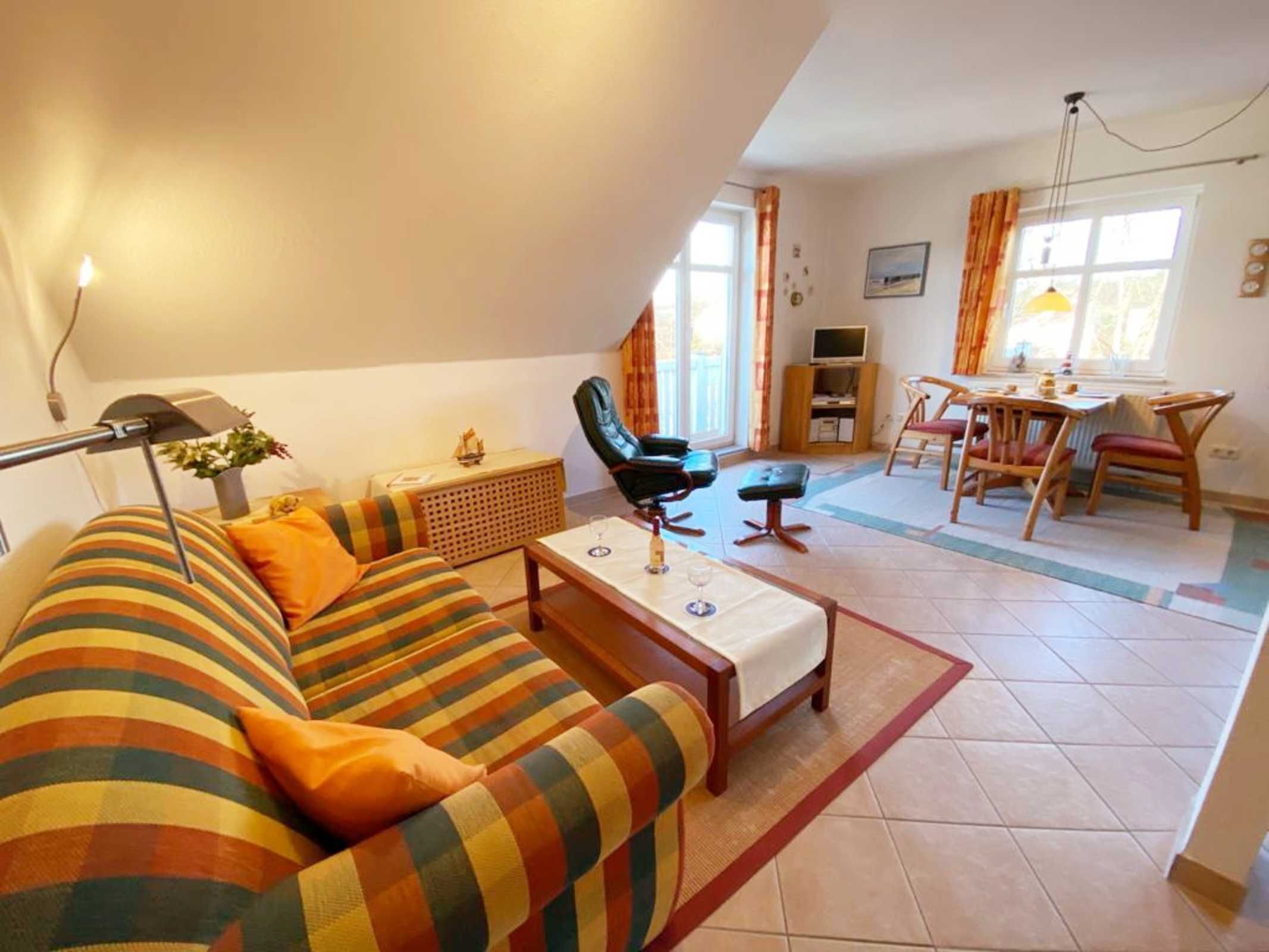 Een gezellige woonkamer met een gestreepte bank, een kleine tafel met een glas, en een eethoek met houten stoelen.
