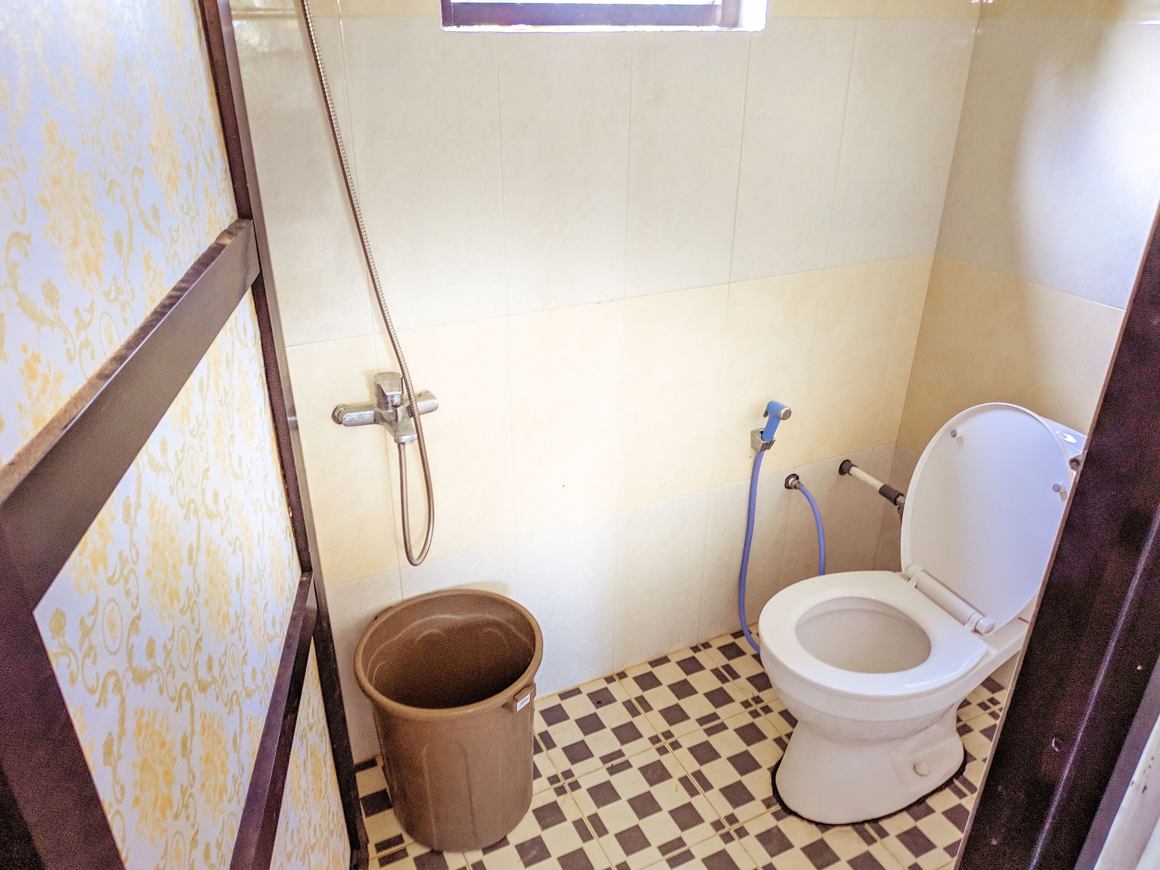 A small bathroom with a toilet, a shower, and a bucket.