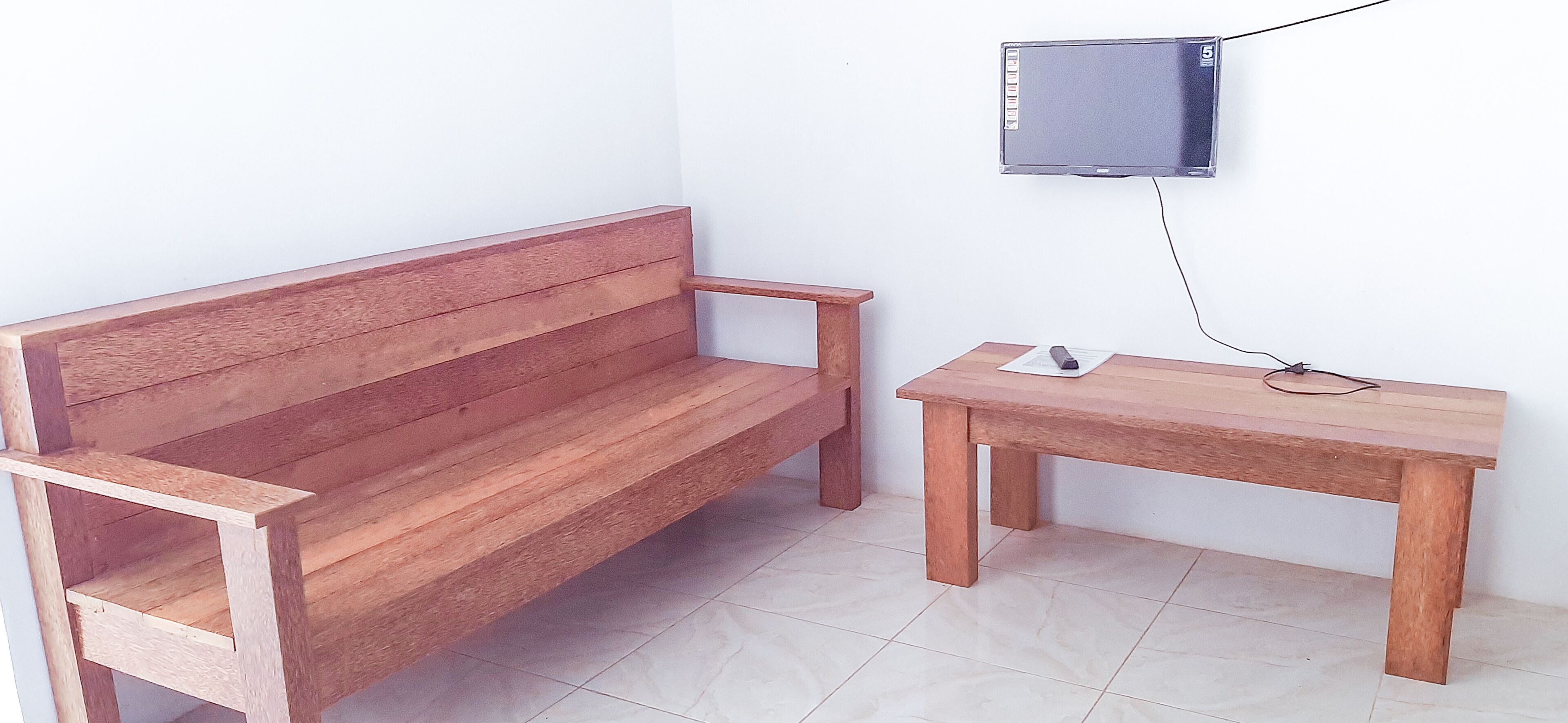 Een houten bank en tafel in een ruimte met een betegelde vloer en een televisie aan de muur.
