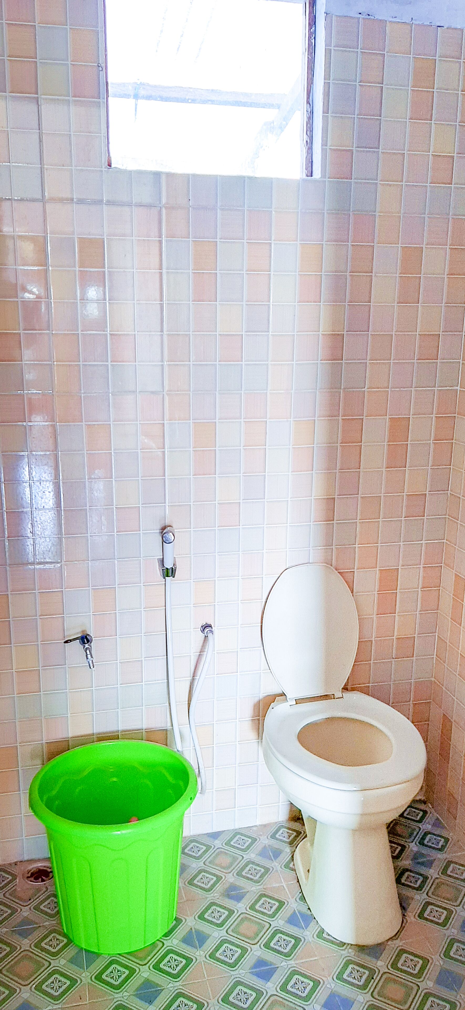 A bathroom with a toilet, a green bucket, and tiled walls.