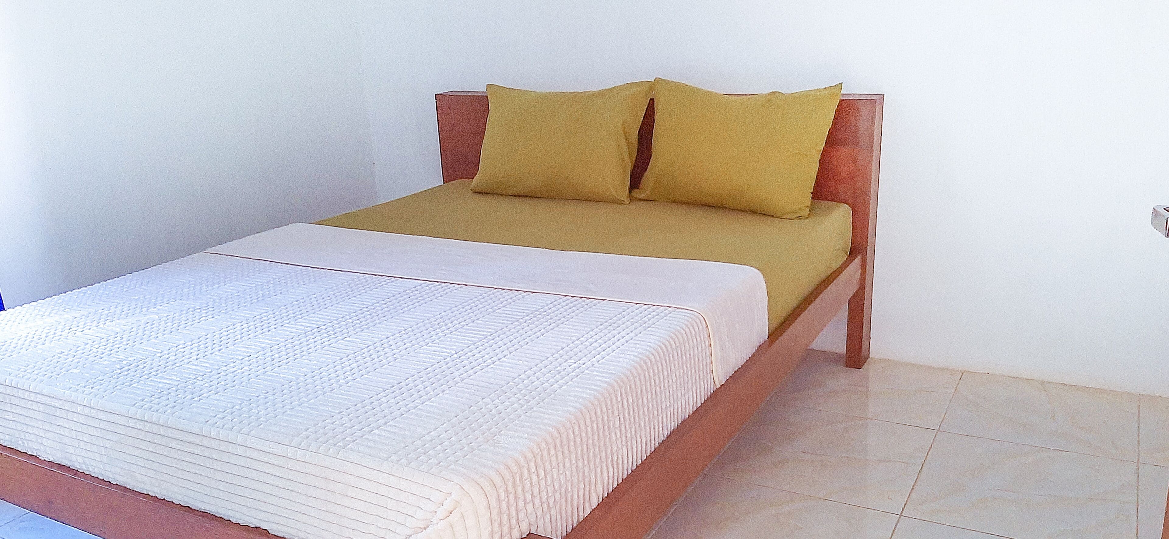 A single bed with a wooden headboard, a white mattress, and two yellow pillows.