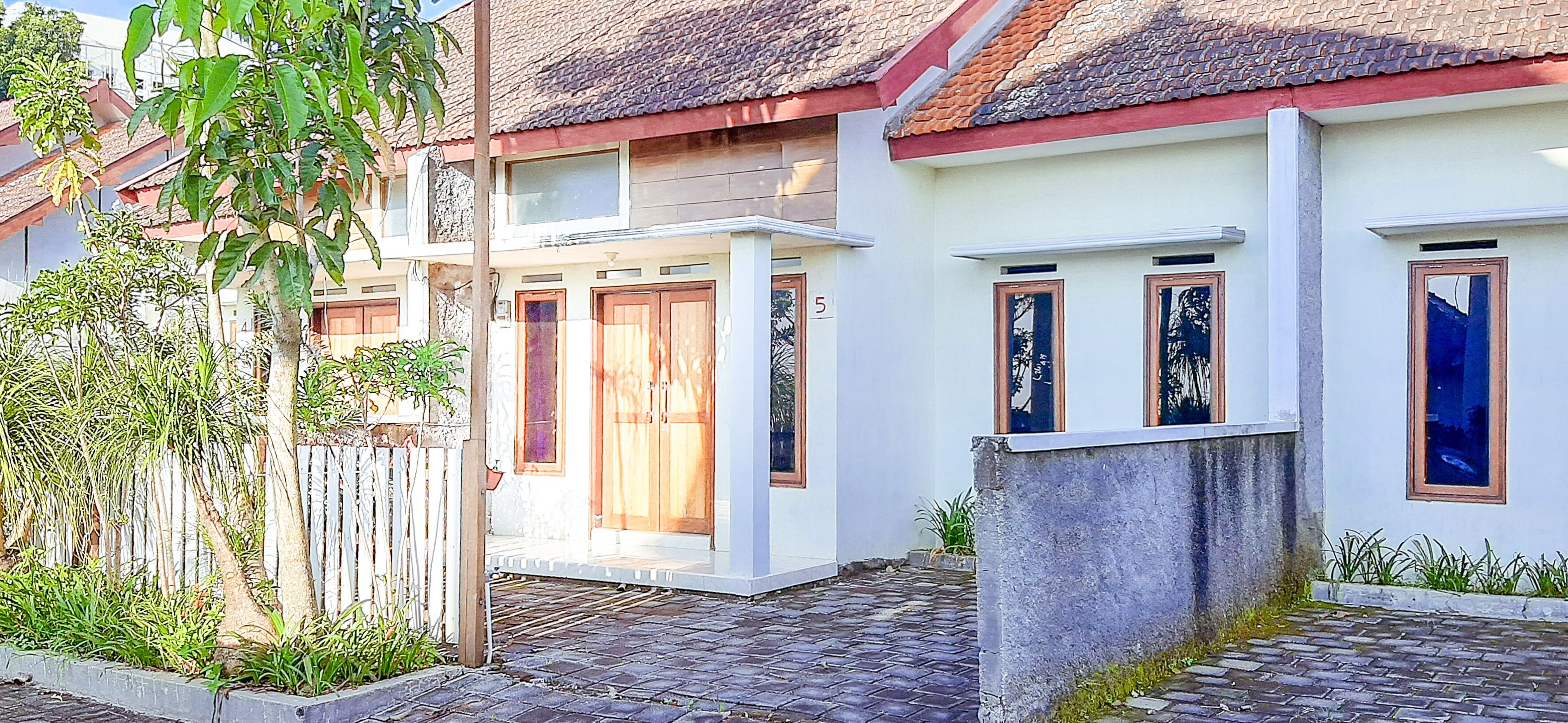 Una casa de dos pisos con techo de tejas, paredes exteriores blancas y una cerca de madera.