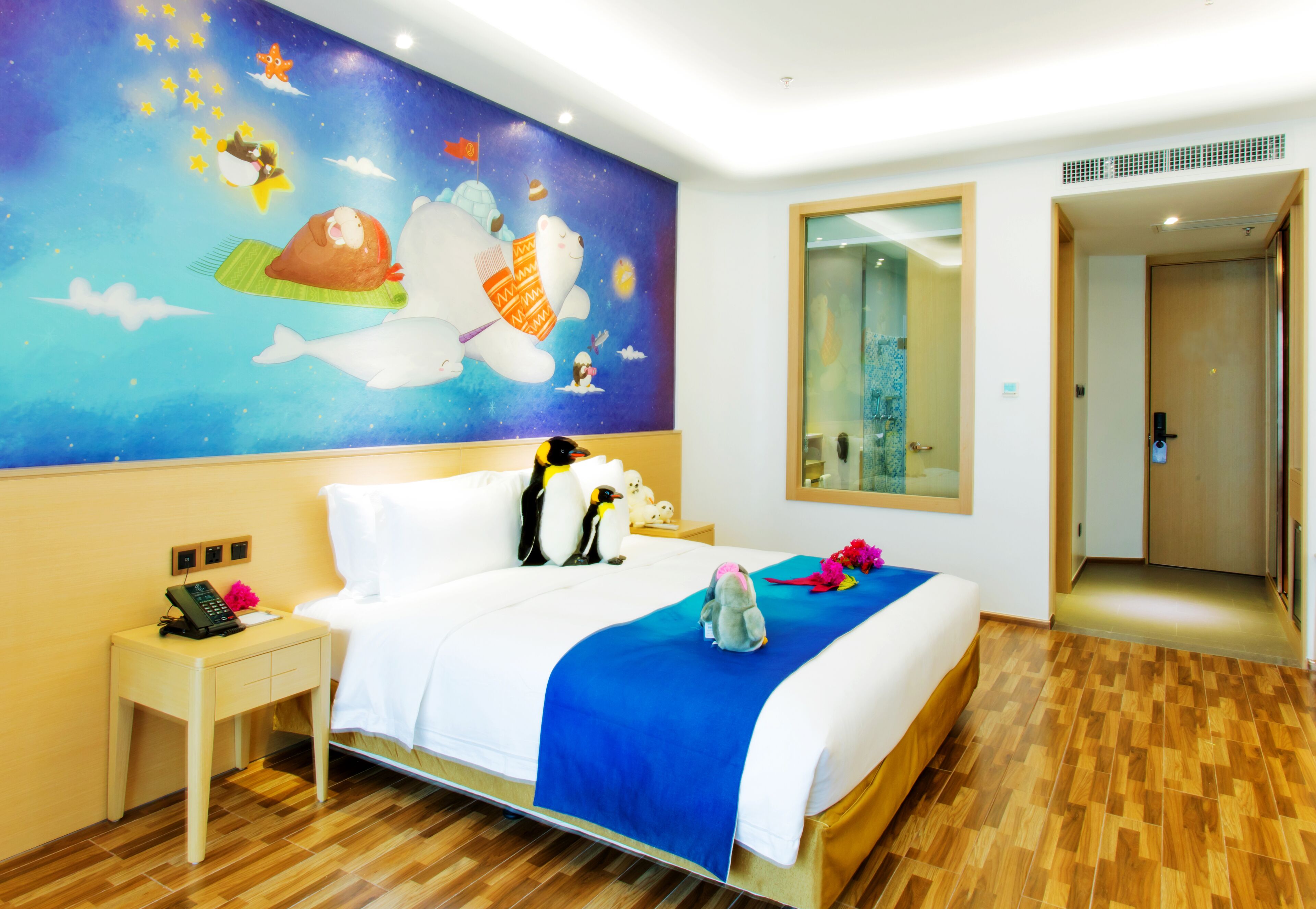 A hotel room with a large bed, a nightstand with a phone, a blue bedspread, and a wall mural.