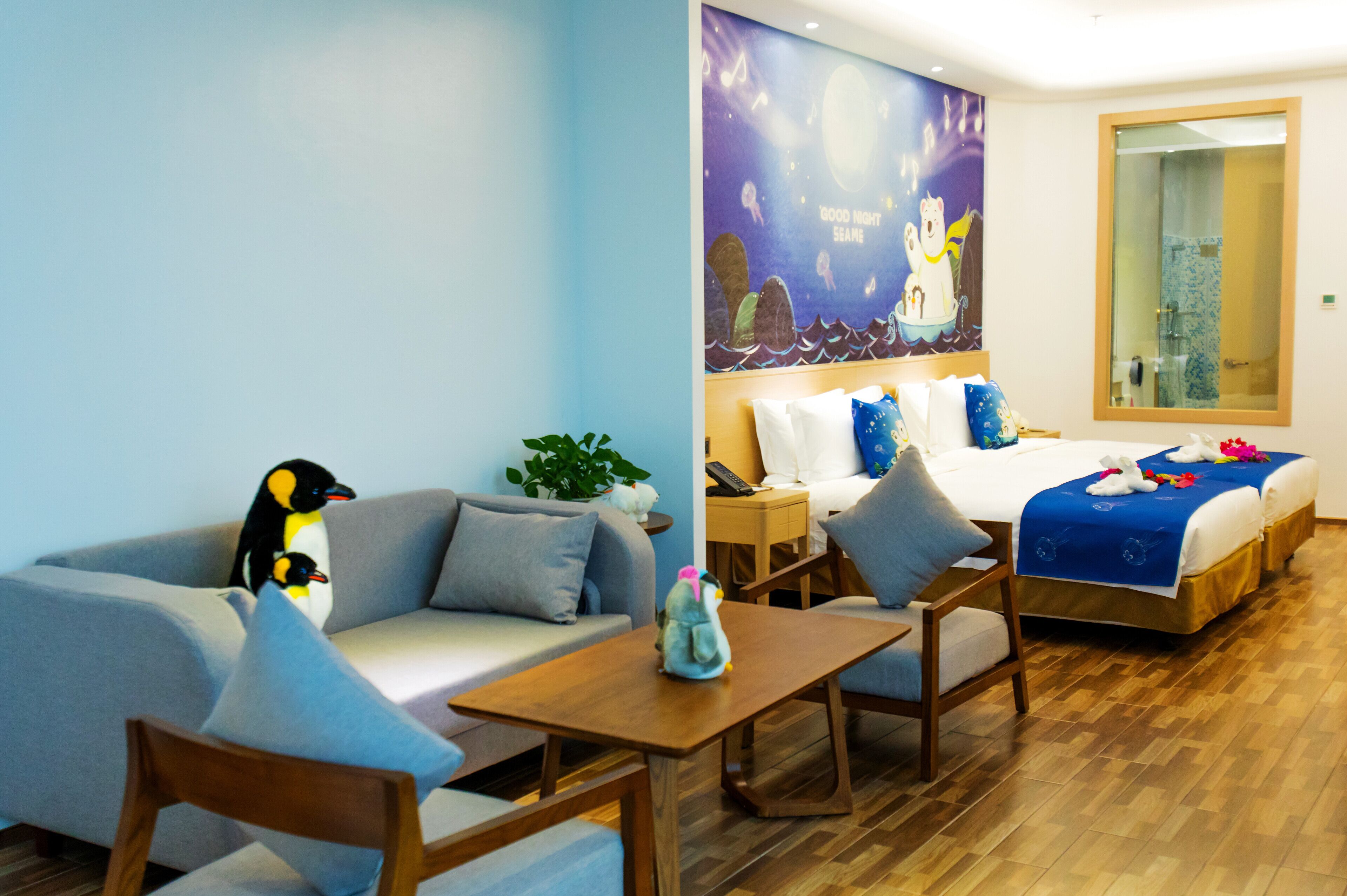 Quarto de hotel com cama, sofá, mesa de madeira e um mural na parede.