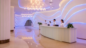 A modern reception area with a curved reception desk, three staff members, and a large, illuminated wall. - Sanya Discovery Ocean World (Sanya)