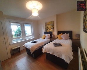 Quarto com duas camas, ventilador de teto, janela e um quadro na parede.